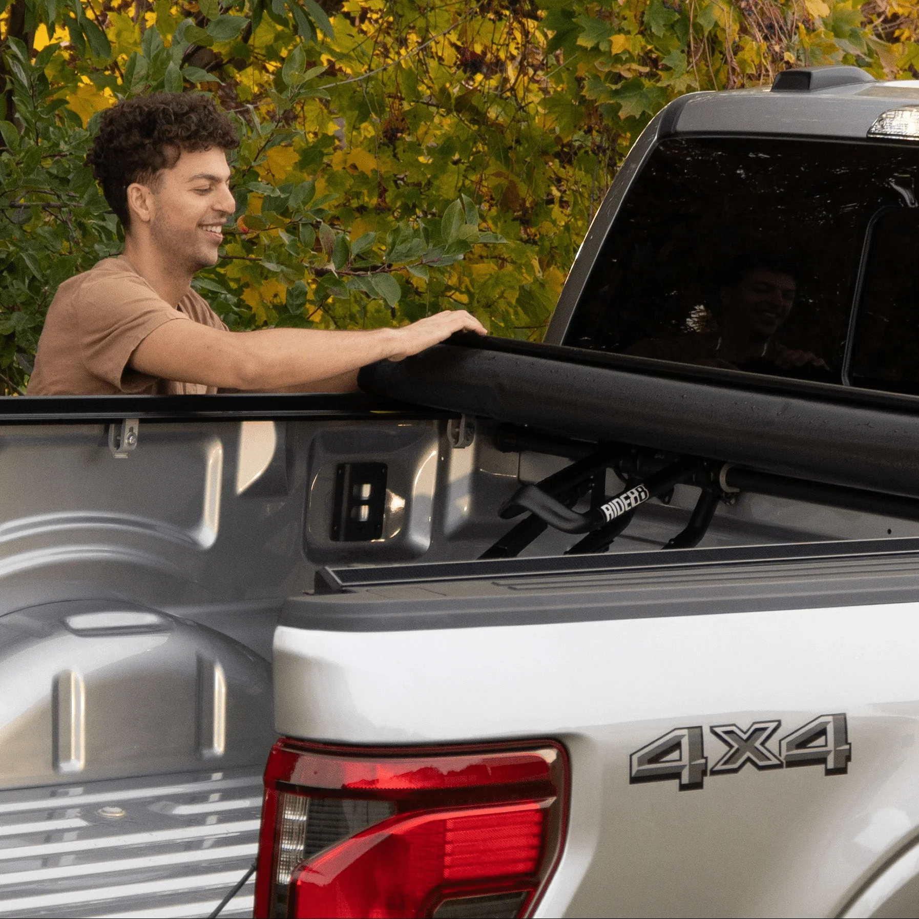 Man closing a tonneau cover over a truck bed with a QR3 bike rack inside.